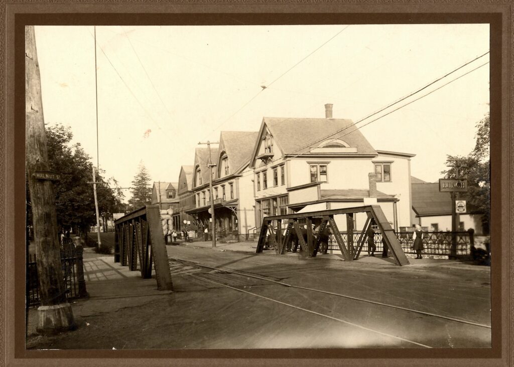 The 1872 Main Street bridge, standing on Walnut Street and looking west. The farthest building was "Assabet House", a large boarding house demolished in 1962 to make room for the present-day post office, which opened in 1963. Photo courtesy of Maynard Historical Society